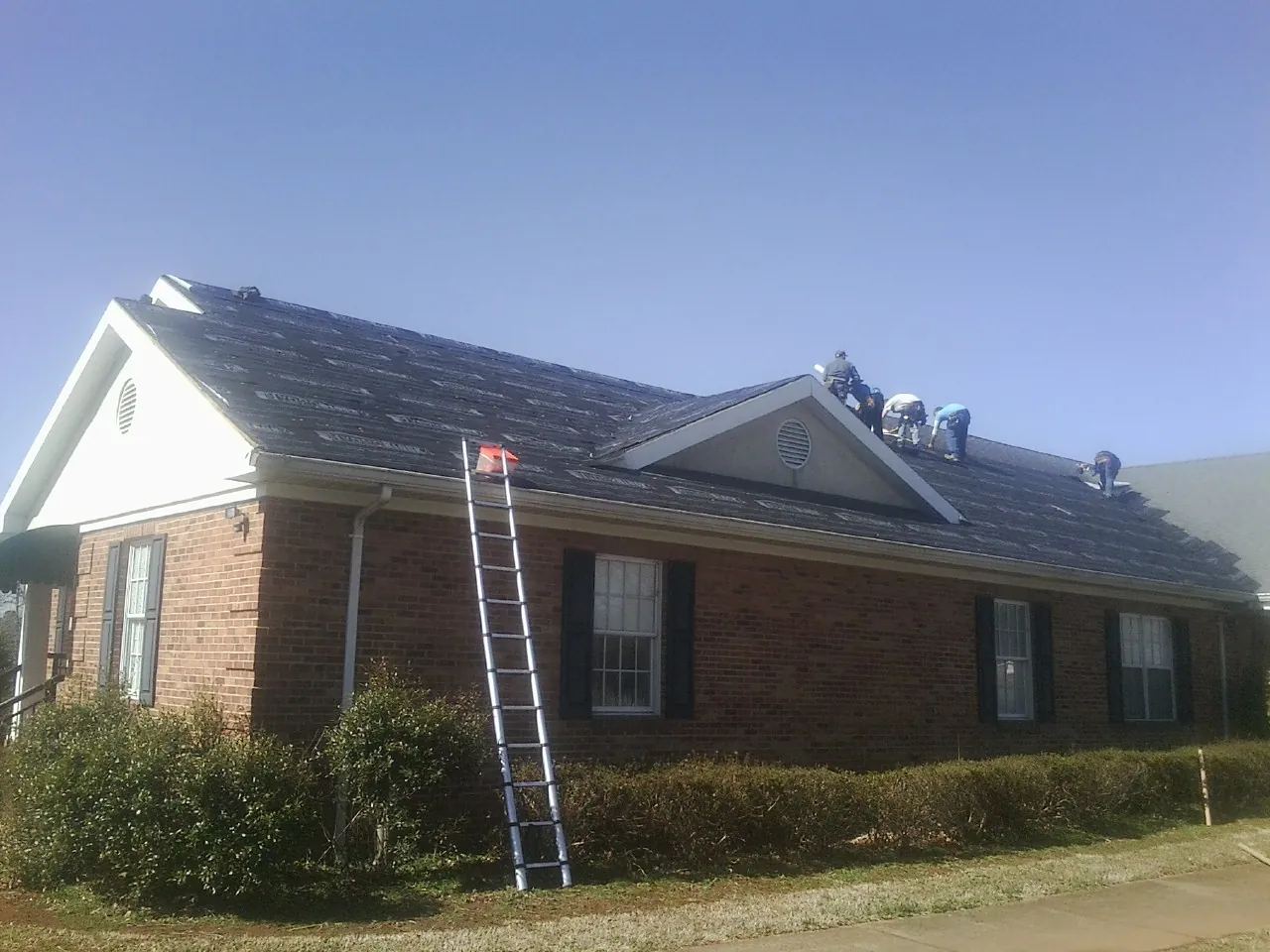 Crew tearing shingles off a brick ranch roof with a ladder set — Metal Roof Repair work by our crew in Turtletown