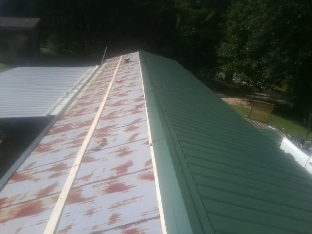 Old rusted panels beside newly installed green metal roofing — Wind Damage Roof Repair by Roofing Brothers in Turtletown
