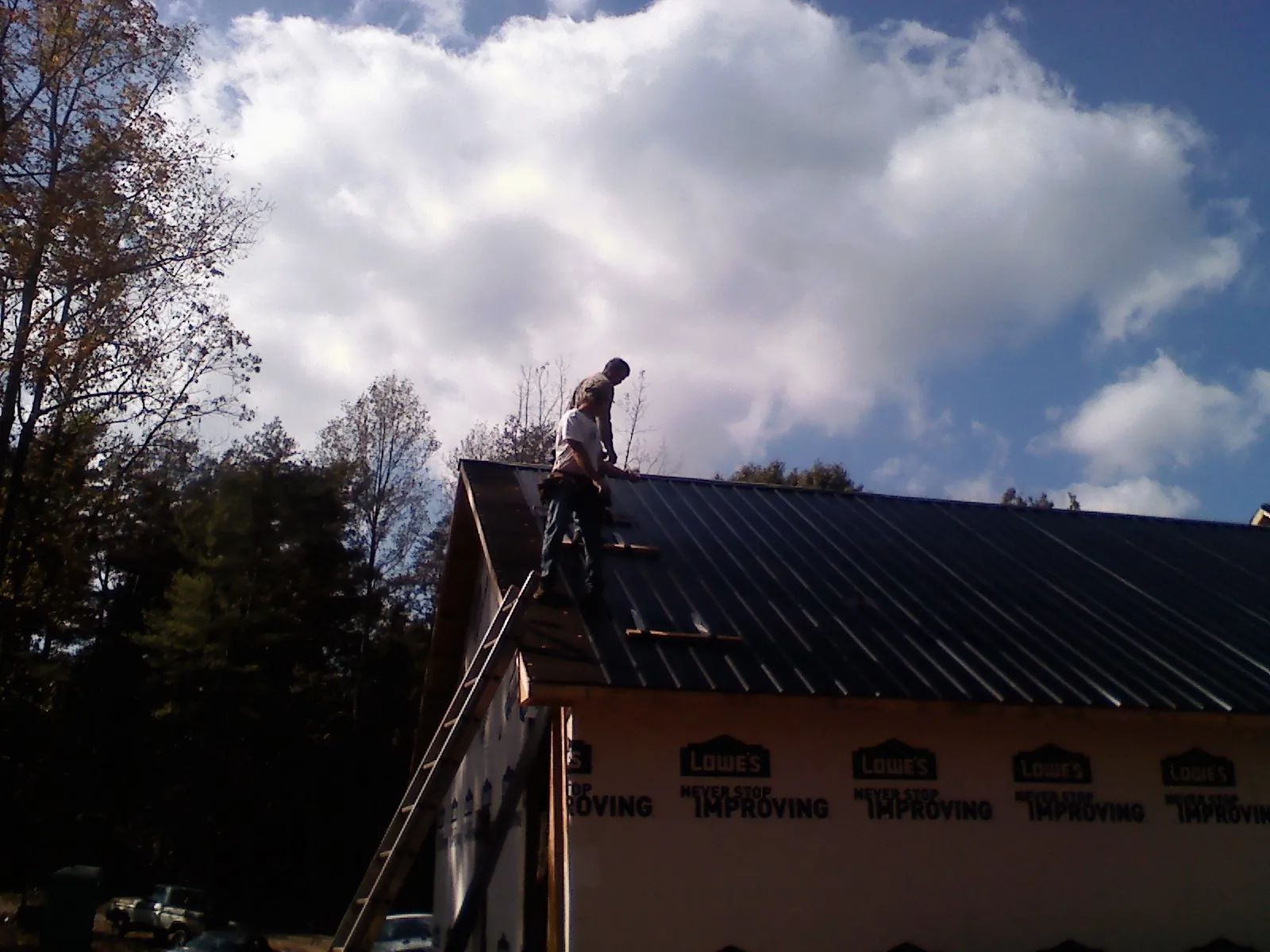 Roofer fastening dark metal panels high against a cloudy sky, from a Roof Inspection job in Turtletown