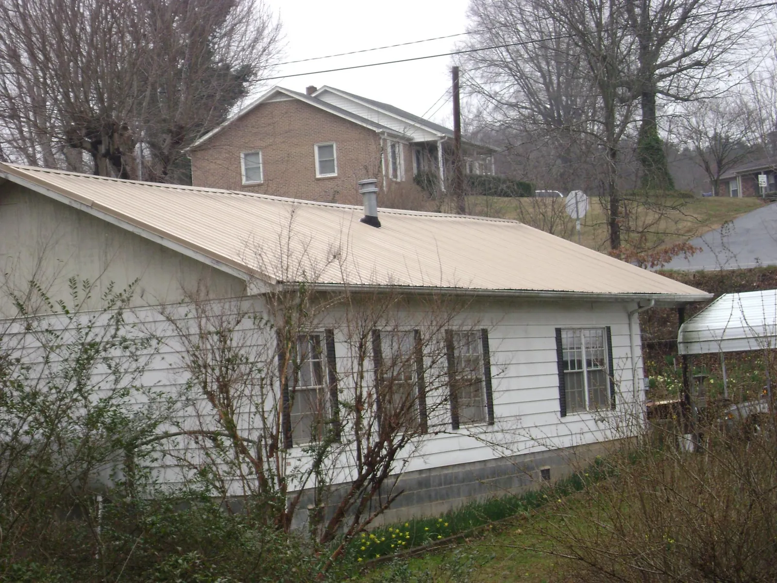 Tan metal roof on a white sided house set into a hillside — Commercial Roofing by Roofing Brothers in Turtletown